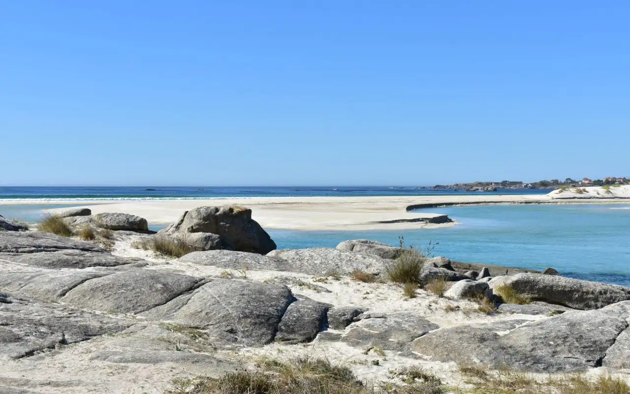 Playa de Carnota en Galicia, arena blanca y rocas de granito con agua turquesa y cielo azul