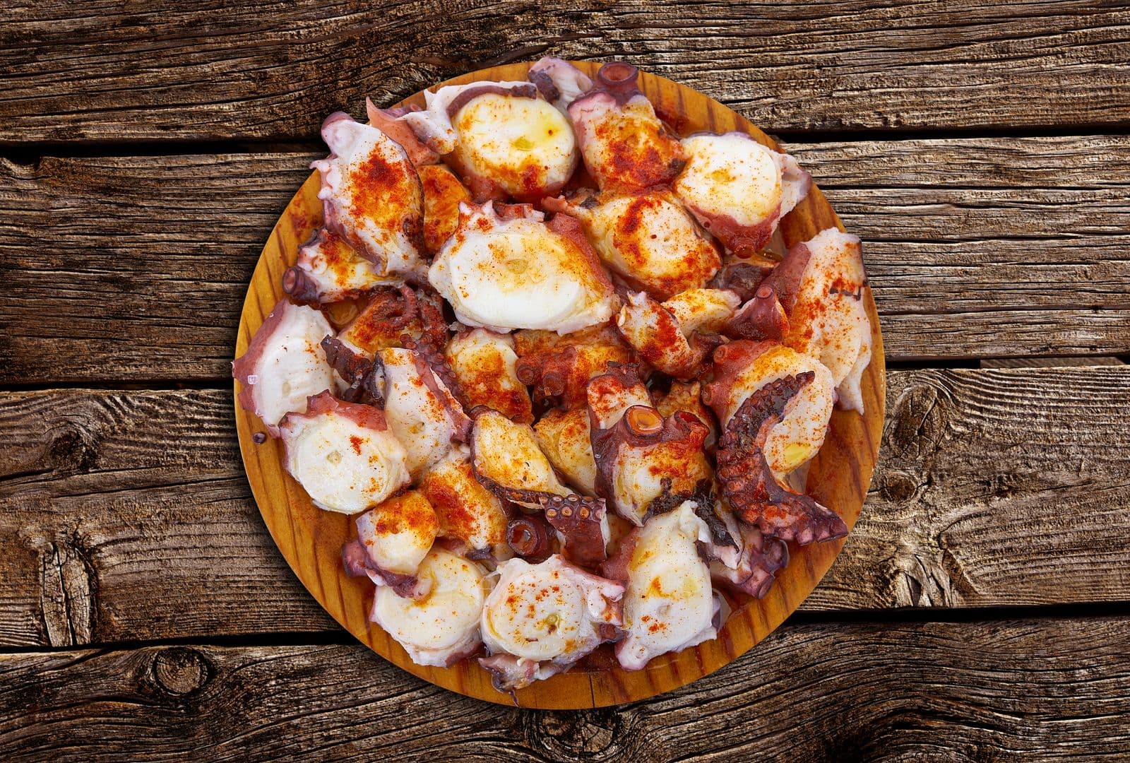 Pulpo a feira servido en plato de madera con pimentón y aceite